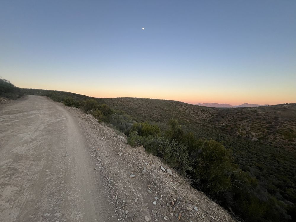 A dirt road at dusk with the moon rising over distant mountains